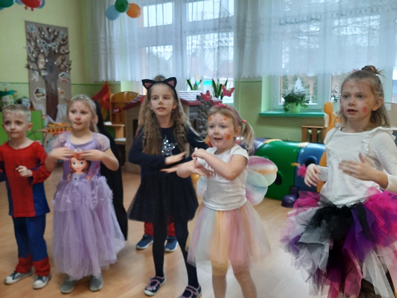 Dziewczynki w bajecznie kolorowych i fantazyjnych strojach tańczą  w sali lekcyjnej
