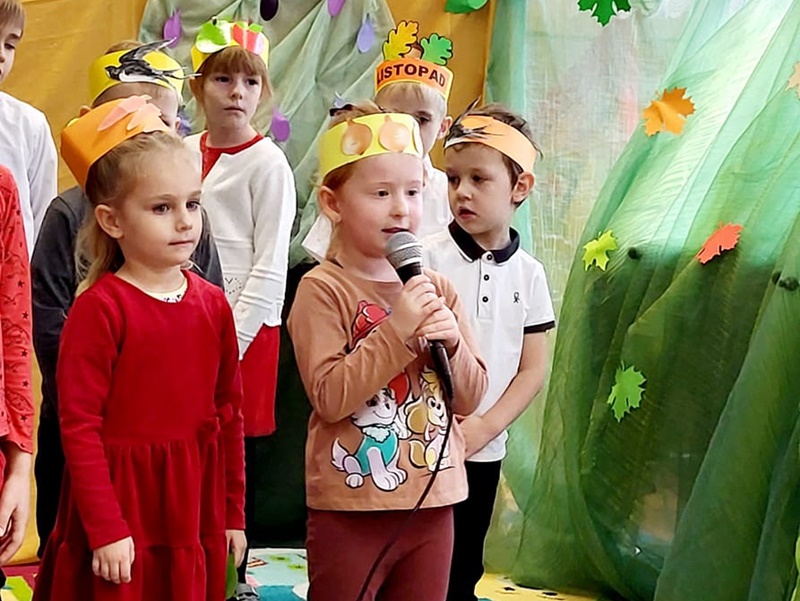 Czworo dzieci z kolorowymi opaskami na głowach. Stoją na scenie, która ma jesienny wystrój.