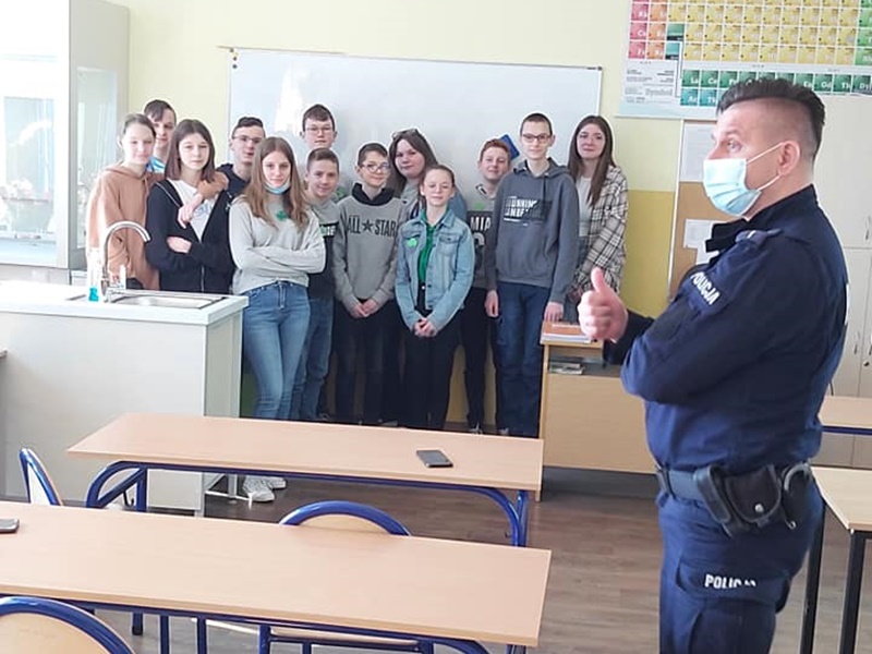 Policjant stoi przed grupą uczniów w sali lekcyjnej