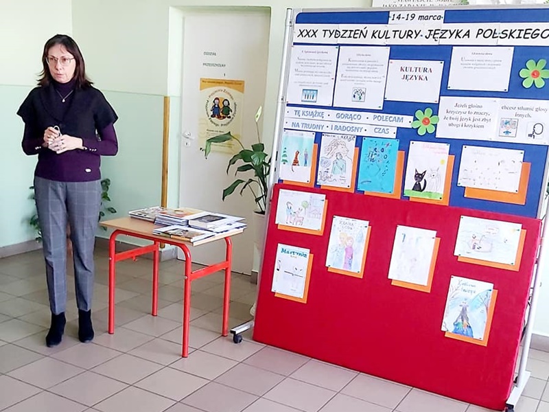 Uczennica stoi obok gazetki na korytarzu szkolnym poświęconej Tygodniowi Kultury Języka Polskiego